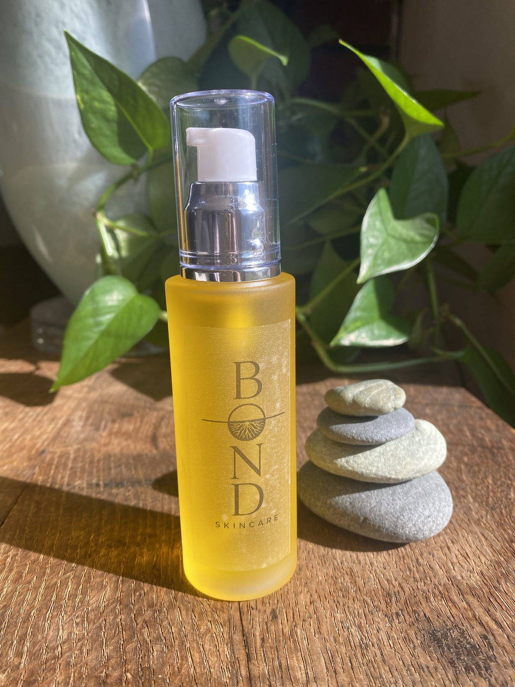 Bond Recovery Oil in a large amber pump bottle on a wooden table beside stacked stones and a leafy plant