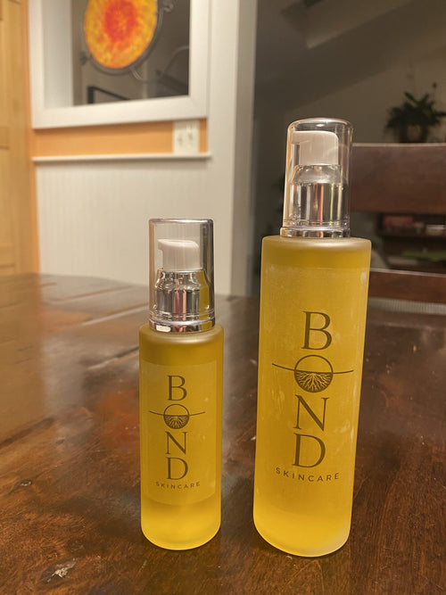 Bond Recovery Oil in its small 2 oz and large 4 oz pump bottles side by side on a wooden table